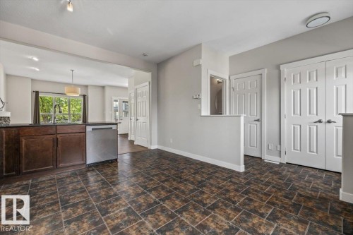 Spacious open-concept area featuring durable tile flooring, rich wood-finish cabinetry, a stainless steel dishwasher, and multiple paneled doors - 356 Pioneer Road, Spruce Grove, AB 