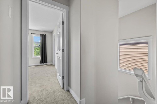 Carpeted hallway with a white trim doorway opening to a room with a large window - 356 Pioneer Road, Spruce Grove, AB 