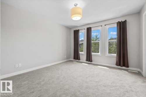 Carpeted room with light gray walls, featuring three windows with dark curtains, white trim, and a ceiling-mounted drum light fixture - 356 Pioneer Road, Spruce Grove, AB 