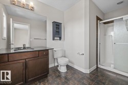 Bathroom featuring a dark wood-finish vanity with a dark countertop, an integrated sink, and a large wall-mounted mirror - 