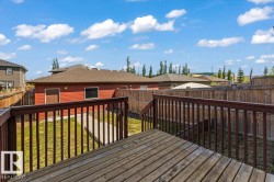 Spacious backyard featuring a wooden deck with railing, a red-sided detached structure with a brown shingled roof, a concrete pathway, and wooden perimeter fencing - 