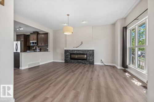 Spacious living area featuring wood-finish flooring, a stone-clad fireplace with an electric insert, and a large multi-pane window - 356 Pioneer Road, Spruce Grove, AB 