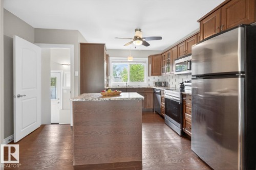 Kitchen featuring wood-finish flooring, an island with a stone countertop, wood cabinetry, stainless steel appliances, and a tiled backsplash - 9815 68 Avenue, Edmonton, AB - Indoor Photo Showing Kitchen With Stainless Steel Kitchen