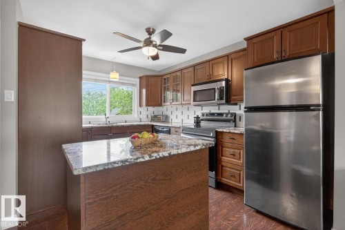 Kitchen featuring a central island with a stone countertop, rich wood-finish cabinetry, stainless steel appliances, a white subway tile backsplash, and wood-finish flooring - 9815 68 Avenue, Edmonton, AB - Indoor Photo Showing Kitchen With Stainless Steel Kitchen