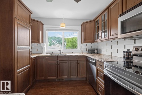 Kitchen featuring wood-finish flooring, dark wood cabinetry, light-toned countertops, a white subway tile backsplash, and stainless steel appliances - 9815 68 Avenue, Edmonton, AB - Indoor Photo Showing Kitchen