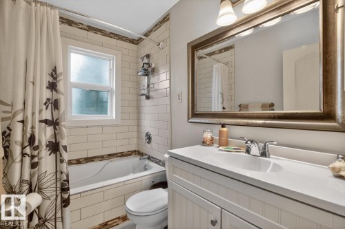 Bathroom featuring a white vanity with a single sink, an ornate framed mirror, and a tub-shower combination - 9815 68 Avenue, Edmonton, AB - Indoor Photo Showing Bathroom