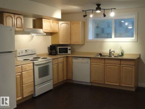 Kitchen featuring wood-finish cabinetry, laminate countertops, a double basin sink, and a full suite of white appliances including a refrigerator, range, and dishwasher - 9815 68 Avenue, Edmonton, AB - Indoor Photo Showing Kitchen With Double Sink