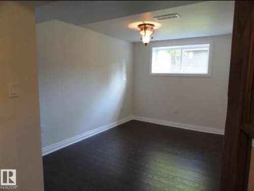 Spacious room with dark wood-finish flooring, crisp white baseboards, and neutral wall tones - 9815 68 Avenue, Edmonton, AB - Indoor Photo Showing Other Room