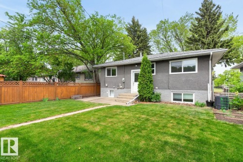 Expansive backyard featuring a manicured lawn, full wood privacy fence, concrete patio, exterior access, and a stucco finish on the property - 9815 68 Avenue, Edmonton, AB - Outdoor