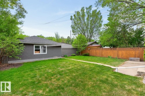Expansive rear yard featuring a manicured lawn, a concrete pathway, a wood privacy fence with lattice detailing, and mature perimeter trees - 9815 68 Avenue, Edmonton, AB - Outdoor