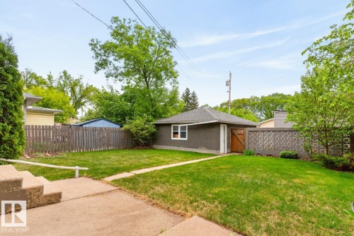 Detached garage with stucco exterior and wood door, complemented by a decorative block fence - 9815 68 Avenue, Edmonton, AB - Outdoor