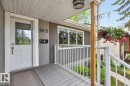 Inviting front porch featuring a white entry door with decorative glass, stucco and stacked stone exterior accents, a dark gray porch deck, and white railings - 9815 68 Avenue, Edmonton, AB  - Outdoor With Exterior 