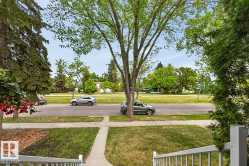 Front yard featuring a concrete walkway, green lawn, white railing, and mature trees - 9815 68 Avenue, Edmonton, AB - Outdoor With View