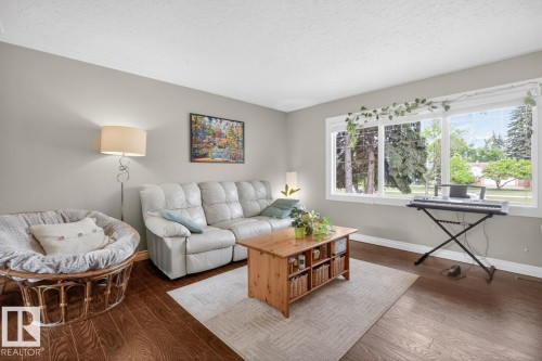 Spacious living area featuring large windows, wood-finish flooring, light grey walls, and white baseboards - 9815 68 Avenue, Edmonton, AB - Indoor Photo Showing Living Room