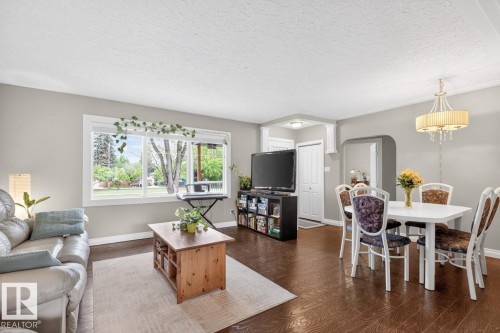 Spacious living area featuring dark wood-finish flooring, a large window providing ample natural light, and light gray wall paint throughout - 9815 68 Avenue, Edmonton, AB - Indoor Photo Showing Other Room