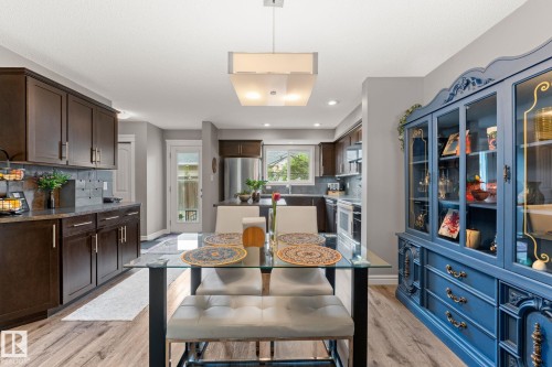 Open-concept dining area with wood-finish flooring, a contemporary chandelier, and a blue decorative hutch - 5813 63 Street, Beaumont, AB 
