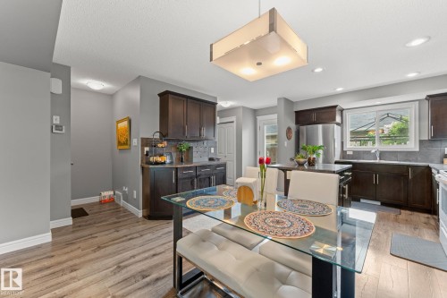 Open-concept kitchen and dining area featuring rich wood cabinetry, stainless steel appliances, wood-finish flooring, and a large window above the sink - 5813 63 Street, Beaumont, AB 