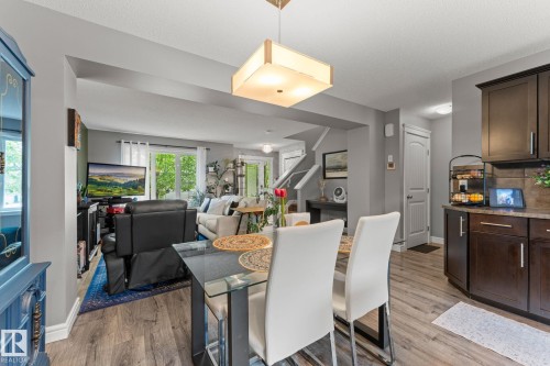 Open-concept living space featuring wood-finish flooring, a contemporary ceiling light fixture, and light gray wall tones - 5813 63 Street, Beaumont, AB 