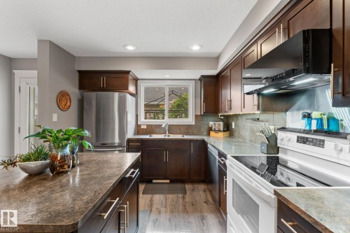 Kitchen featuring abundant dark wood cabinetry, a stainless steel refrigerator, white electric range, and laminate countertops - 5813 63 Street, Beaumont, AB 