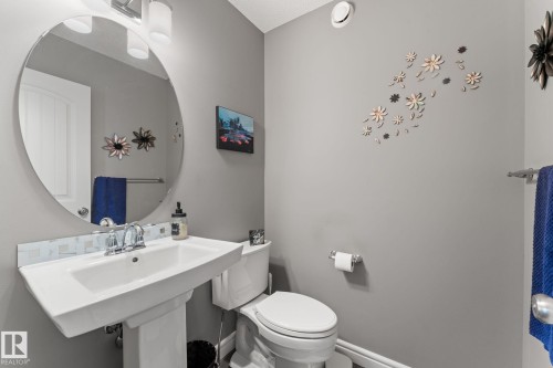 Pedestal sink with chrome faucet, circular mirror, and overhead vanity lighting - 5813 63 Street, Beaumont, AB 