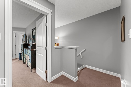 Hallway with neutral carpet flooring and white baseboards, featuring a staircase with a matching white handrail - 5813 63 Street, Beaumont, AB 
