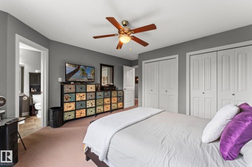 Bedroom featuring neutral carpeting, a ceiling fan with integrated lighting, and two sets of bi-fold closet doors - 5813 63 Street, Beaumont, AB 