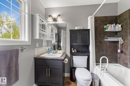 Bathroom featuring a white bathtub, dark brown subway tile shower surround, and a vanity with a white sink, dark cabinetry, and a patterned tile backsplash - 5813 63 Street, Beaumont, AB 