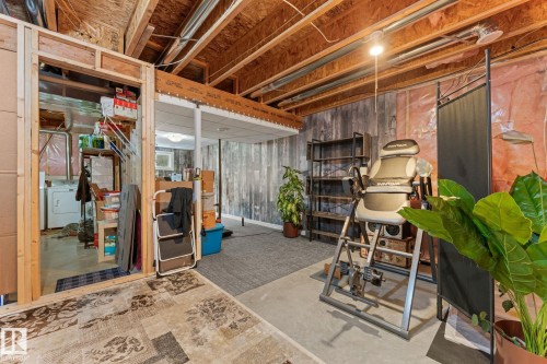 Unfinished basement space featuring exposed wood joists, a framed doorway, and a utility room with a visible washer and dryer - 5813 63 Street, Beaumont, AB 