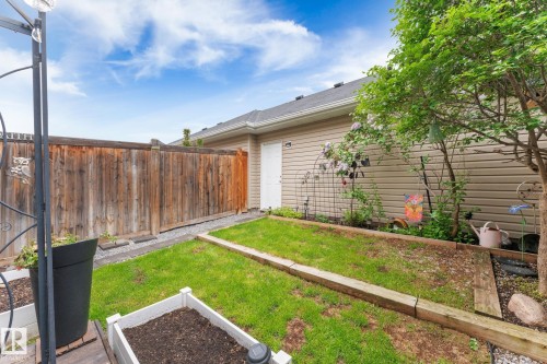 Private outdoor space featuring a wooden privacy fence, a well-defined garden bed, and a small area of green lawn - 5813 63 Street, Beaumont, AB 