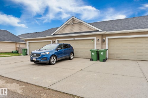 Attached garages with panel doors, concrete driveway, and neutral-toned siding - 5813 63 Street, Beaumont, AB 