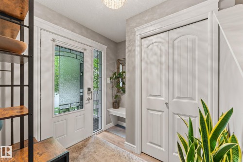 Entryway featuring a decorative frosted glass front door with sidelight, overhead lighting, wood-finish flooring, a bi-fold closet, and crown molding - 5813 63 Street, Beaumont, AB 