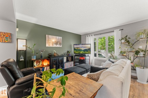 Bright living space featuring wood-finish flooring, a large window with white trim, and a high white ceiling - 5813 63 Street, Beaumont, AB 