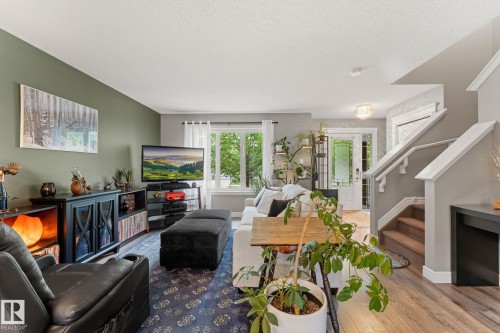 Bright living space featuring a large window, wood-finish flooring, and a carpeted staircase with white railings - 5813 63 Street, Beaumont, AB 