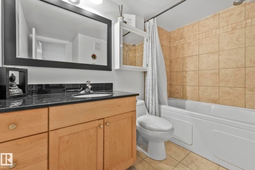 Bathroom featuring a light wood-finish vanity with a dark speckled countertop, an undermount sink, and a black framed mirror - 303 10165 113 Street, Edmonton, AB - Indoor Photo Showing Bathroom
