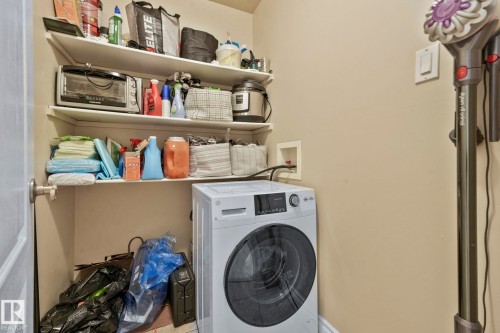 Dedicated laundry area featuring a front-loading washing machine, overhead shelving, and a neutral wall finish - 303 10165 113 Street, Edmonton, AB - Indoor Photo Showing Laundry Room
