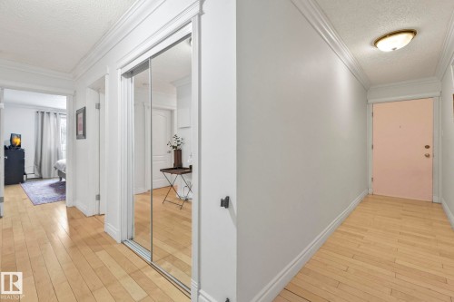Hallway featuring light wood-finish flooring, mirrored sliding closet doors, crown molding, and baseboards - 303 10165 113 Street, Edmonton, AB - Indoor Photo Showing Other Room