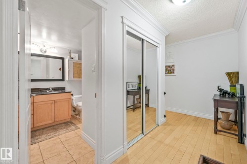Hallway featuring wood-finish flooring, crown molding, and a mirrored closet - 303 10165 113 Street, Edmonton, AB - Indoor