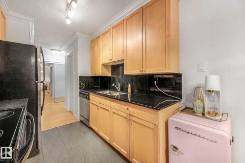 Kitchen featuring wood-finish cabinetry, black stone countertops, and a black tile backsplash - 303 10165 113 Street, Edmonton, AB - Indoor Photo Showing Kitchen