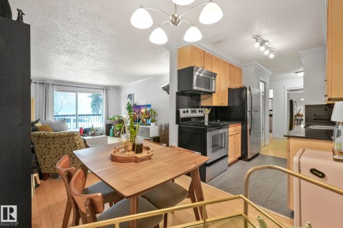 Open-concept living space featuring a dining area with wood-finish flooring, a kitchen with light wood cabinetry, stainless steel appliances, and black countertops, and a living area with a sliding glass door leading to a balcony - 303 10165 113 Street, Edmonton, AB - Indoor