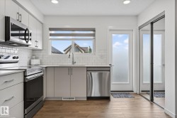 Modern kitchen featuring light gray cabinetry, stainless steel appliances, white subway tile backsplash, and wood-finish flooring - 