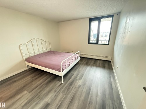 Room featuring neutral painted walls, wood-finish flooring, and a large window with black framing - 706 10125 109 Street, Edmonton, AB 