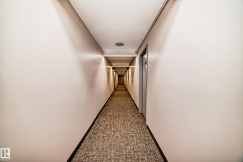 Long hallway featuring neutral-toned walls, recessed ceiling lighting, a textured carpet runner, and multiple entry doors - 706 10125 109 Street, Edmonton, AB 