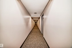 Long hallway featuring neutral-toned walls, recessed ceiling lighting, a textured carpet runner, and multiple entry doors - 