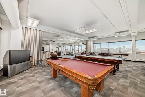 Expansive entertainment area featuring two pool tables, patterned carpet flooring, and abundant natural light from numerous windows - 706 10125 109 Street, Edmonton, AB 