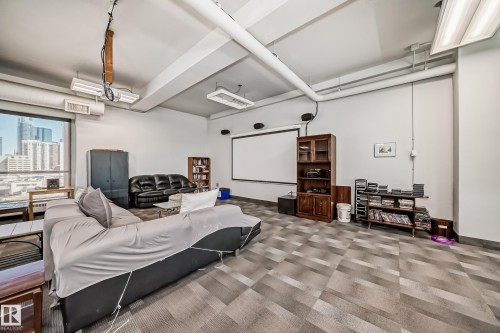 Spacious common area featuring large windows, geometric pattern carpet, exposed overhead ductwork, and a built-in projection screen - 706 10125 109 Street, Edmonton, AB 