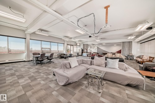 Expansive open-concept room featuring wide windows, patterned carpet flooring, and exposed ceiling ductwork - 706 10125 109 Street, Edmonton, AB 