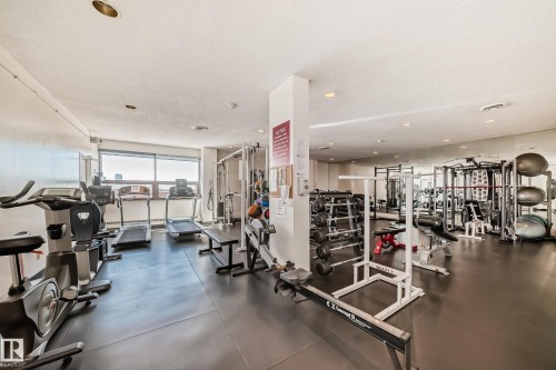 Dedicated fitness center featuring ample cardio equipment, weight training machines, a free weight area, reflective wall panels, and large perimeter windows - 706 10125 109 Street, Edmonton, AB 