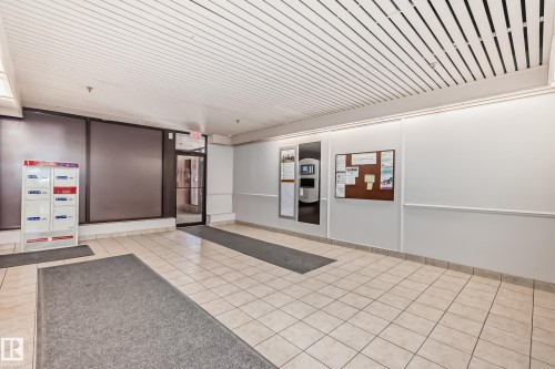 Building entryway featuring light-toned square floor tiles, a grid-patterned ceiling, and an illuminated information board - 706 10125 109 Street, Edmonton, AB 