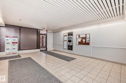 Building entryway featuring light-toned square floor tiles, a grid-patterned ceiling, and an illuminated information board - 