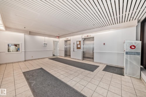 Lobby featuring two stainless steel elevators, white tile flooring, and a slatted ceiling with integrated lighting - 706 10125 109 Street, Edmonton, AB 